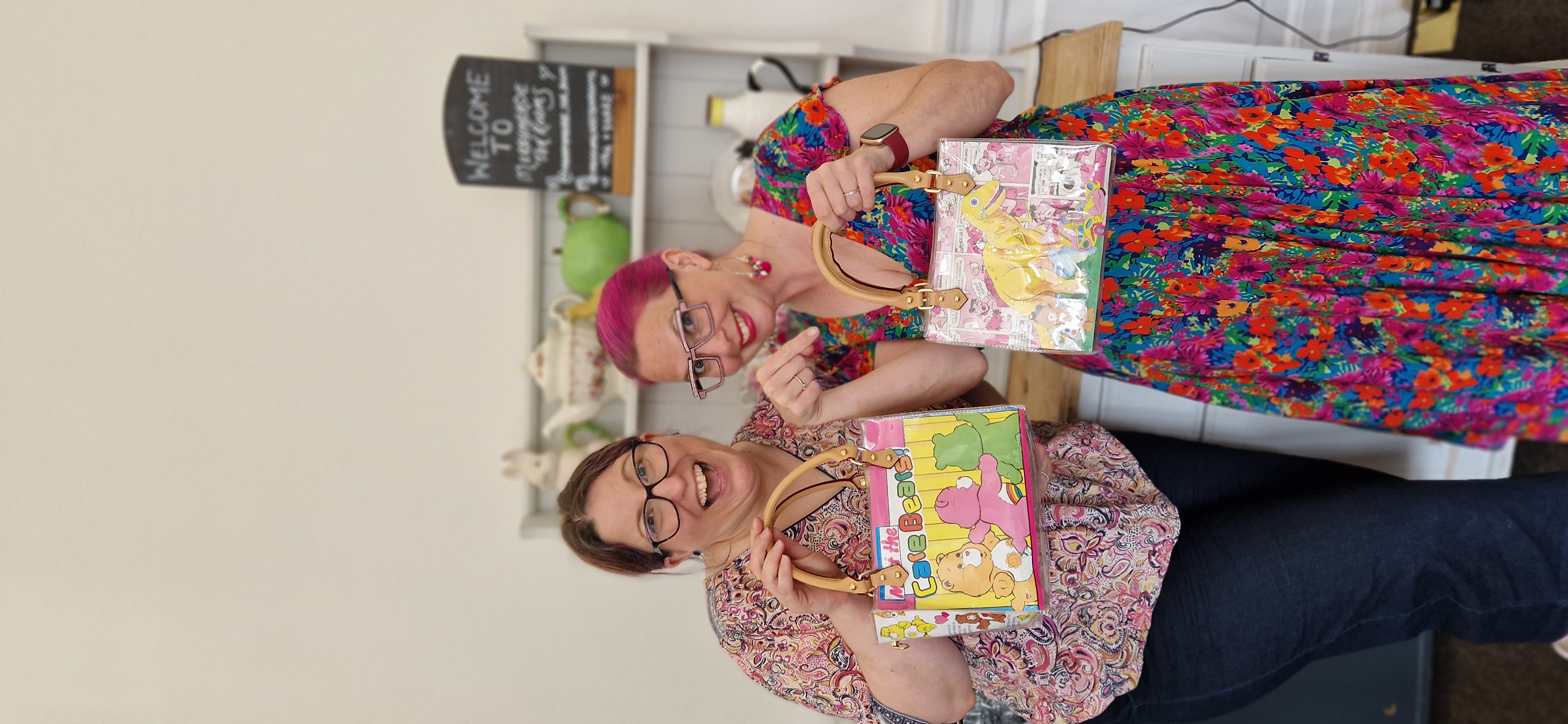 Two women in bright clothing holding quirky handbags they have made
