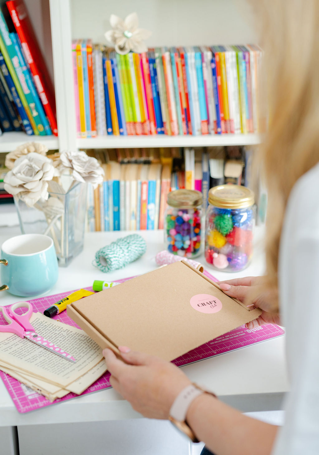 A woman is holding a brown craft kit box filled with new paper crafts