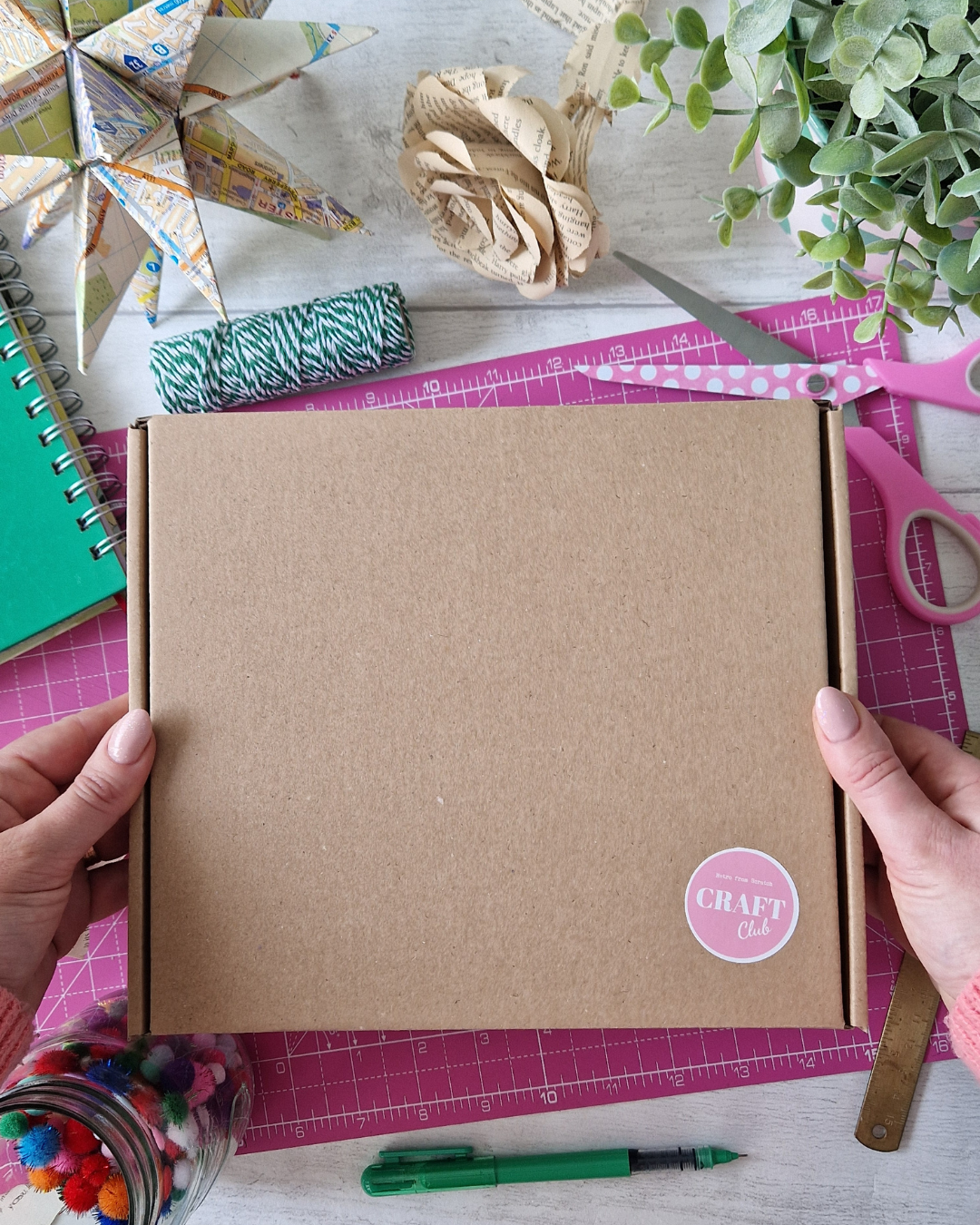 A woman is holding a brown craft kit box filled with new paper crafts