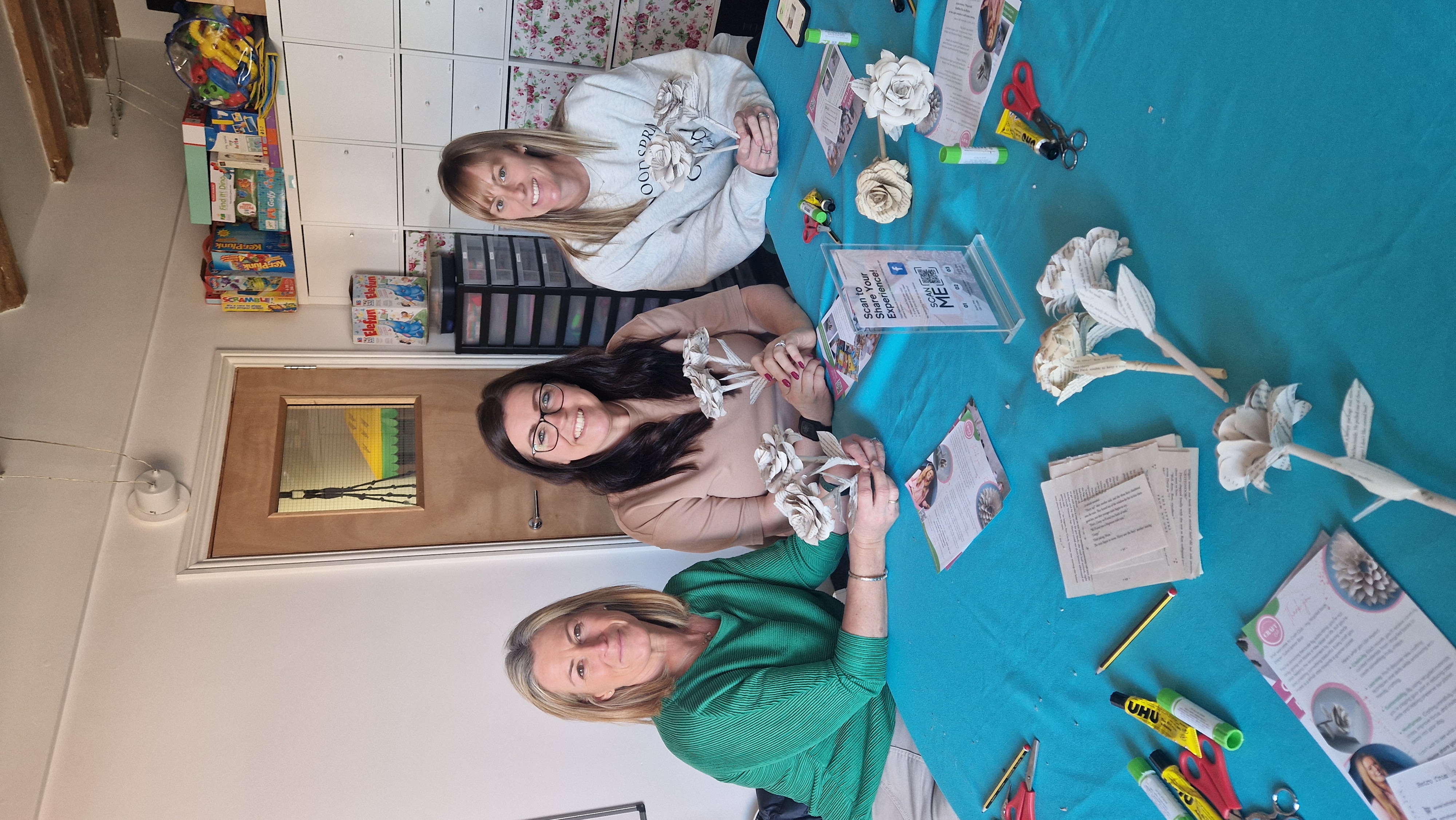 Three women in their 40s holding book paper roses they have made at a craft workshop
